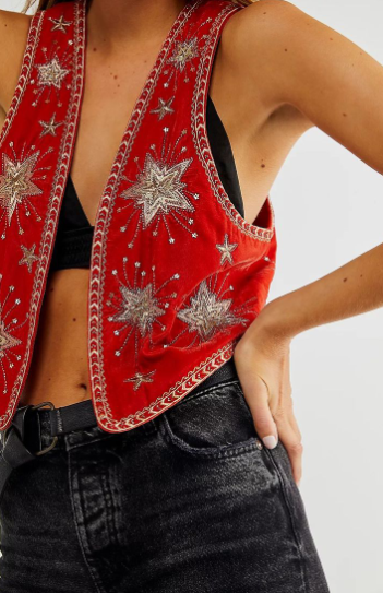 Close-up of a person wearing a vibrant red vest with silver star embroidery, styled over a black bralette and paired with high-waisted black jeans.