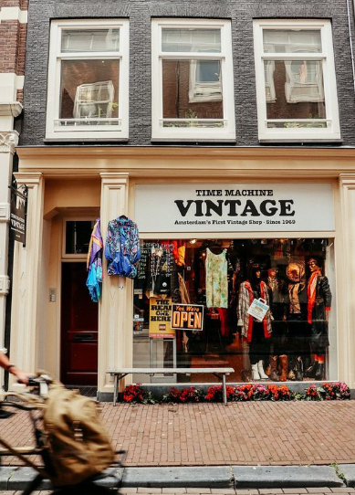 Exterior of “Time Machine Vintage,” a vintage clothing shop with colorful garments displayed outside and a cyclist passing by.
