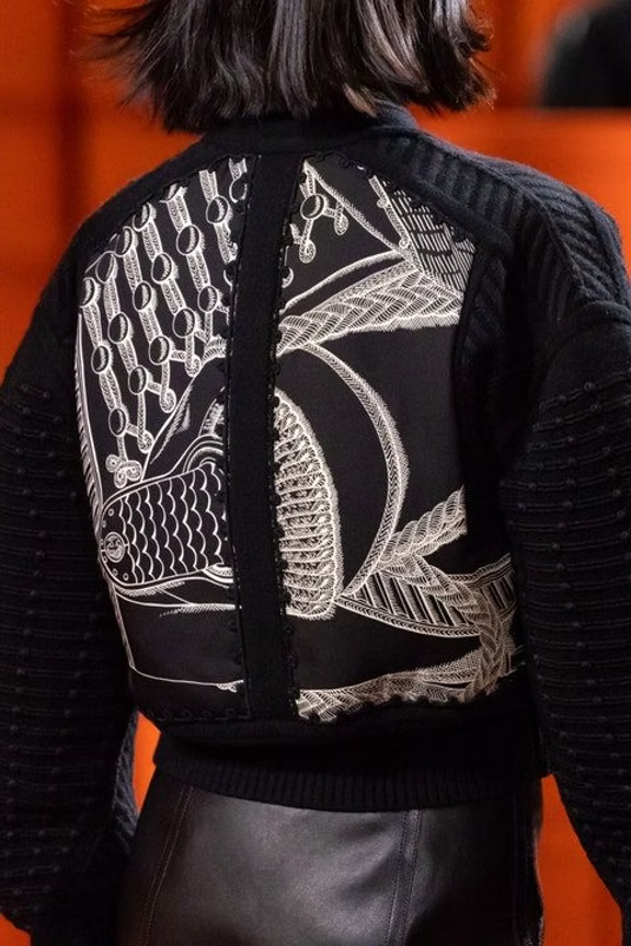 Female model walking the runway in a Hermès black jacket outfit