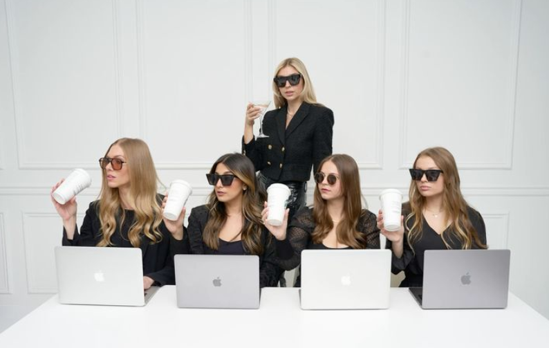 Group of women in sunglasses holding coffee cups while working on laptops, symbolizing digital culture and online content creation.