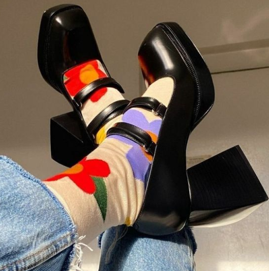 Close-up of black chunky-heeled Mary Jane shoes paired with cream socks featuring colorful floral prints, styled with frayed hem blue jeans.