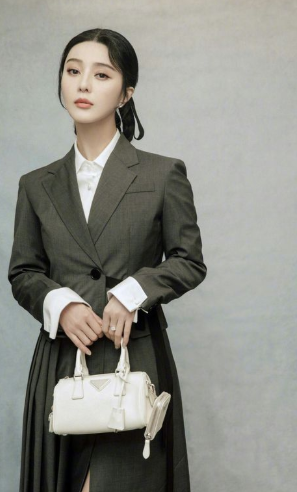 Woman in a tailored suit holding a small white handbag with an elegant, minimal design.