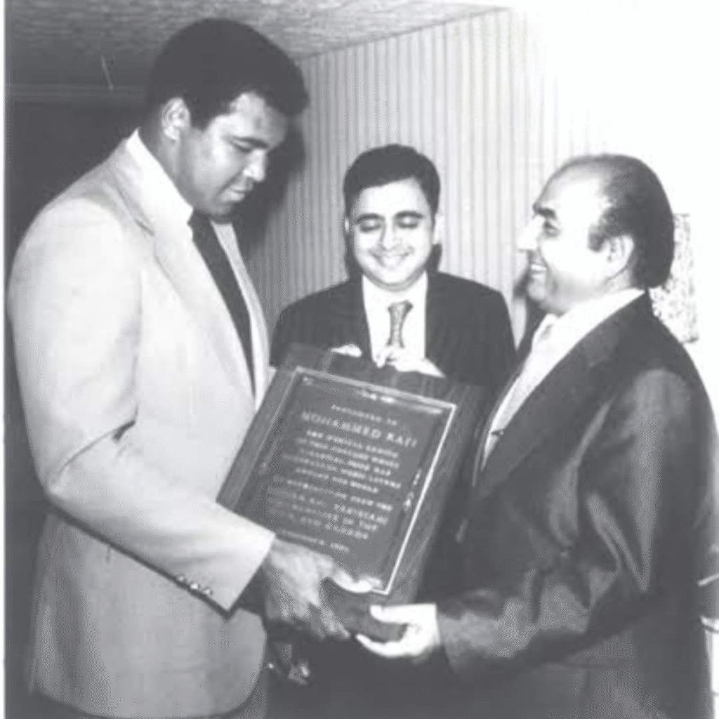 A black-and-white photo showing a tall man in a suit presenting a plaque to another smiling man in formal wear, with a third man standing in the middle holding the plaque.